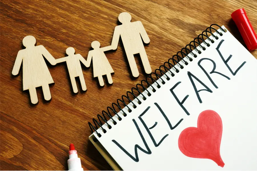 Wooden family figures holding hands beside a notebook with the word welfare and a red heart